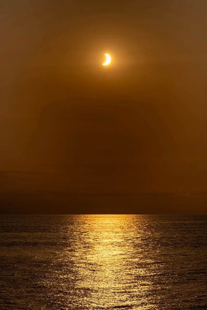 The partly eclipsed sun hanging low over the Atlantic with a path of light across the water